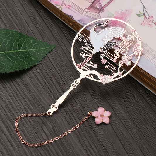 Chinese fan shaped metal bookmark with crane design on a wooden surface
