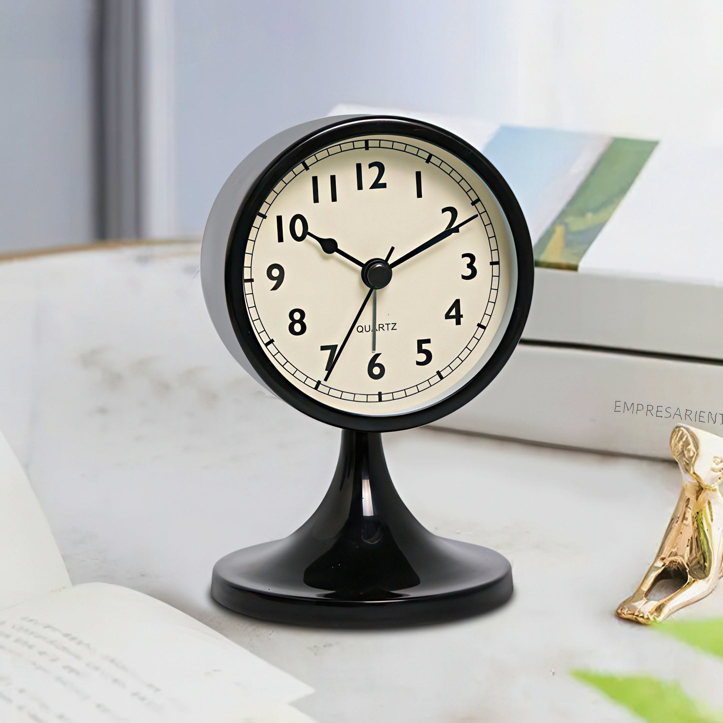Black table clock on a surface with books and a figurine in the background