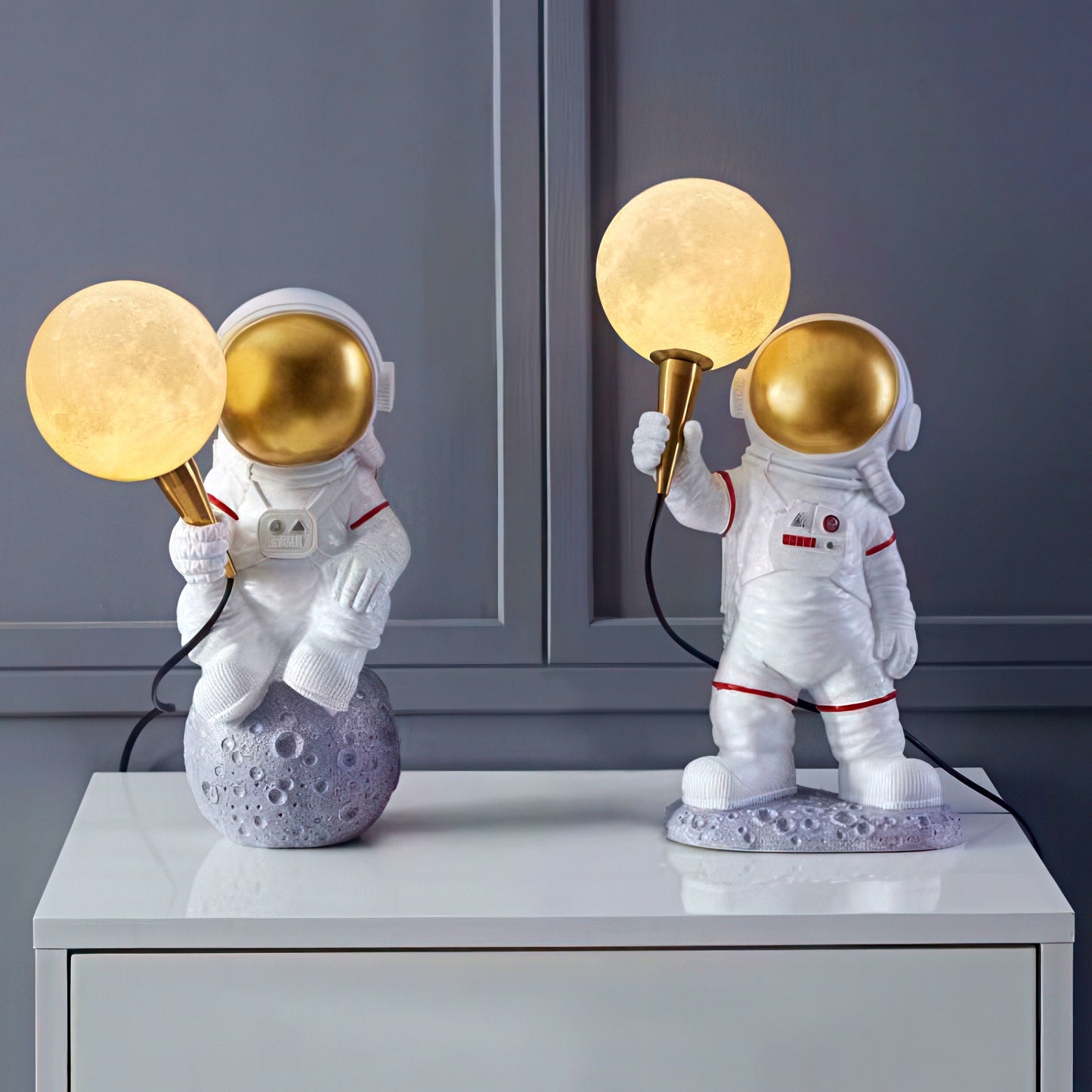 Two astronaut-themed lamps with gold light bulbs on a gray surface.