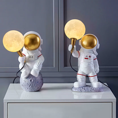 Two astronaut-themed lamps with gold light bulbs on a gray surface.