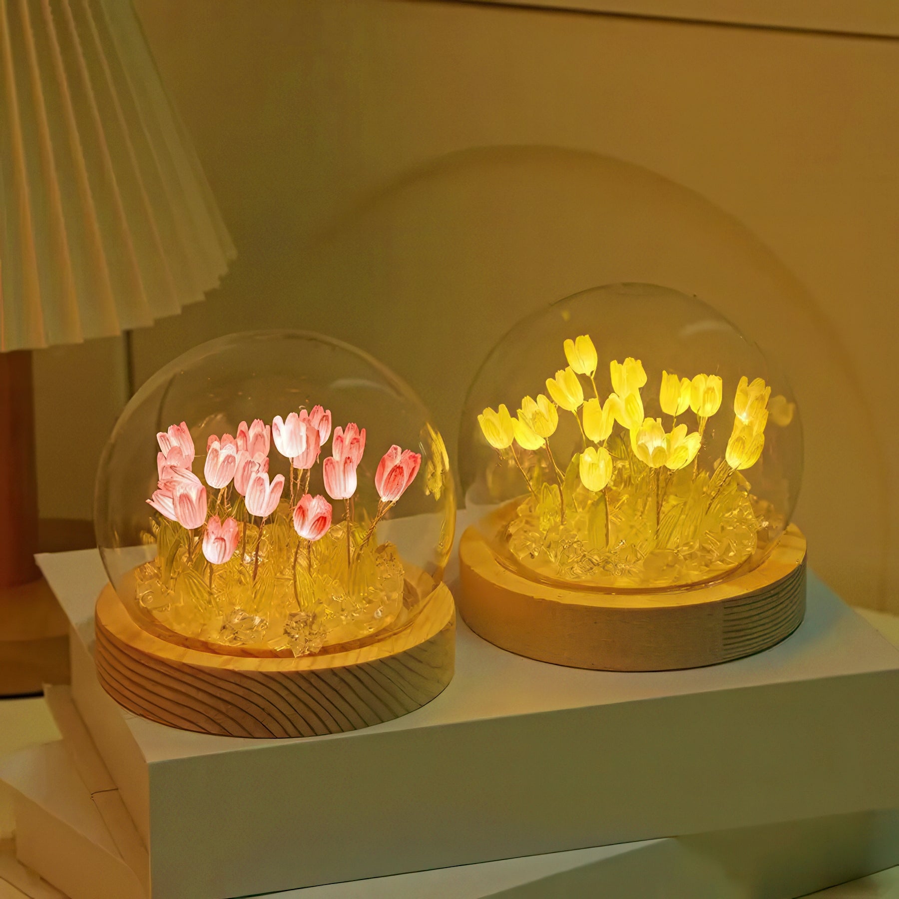 Two glass domes with LED flowers with a wooden base on a white surface.