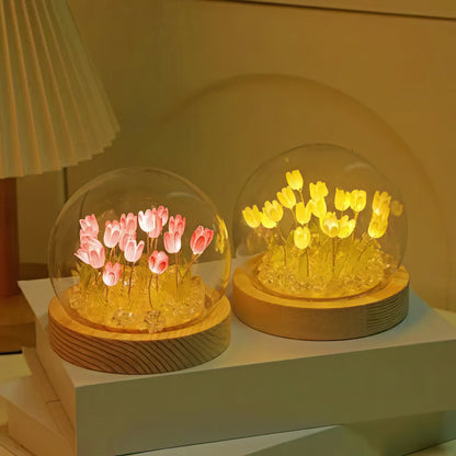 Two glass domes with LED flowers with a wooden base on a white surface.