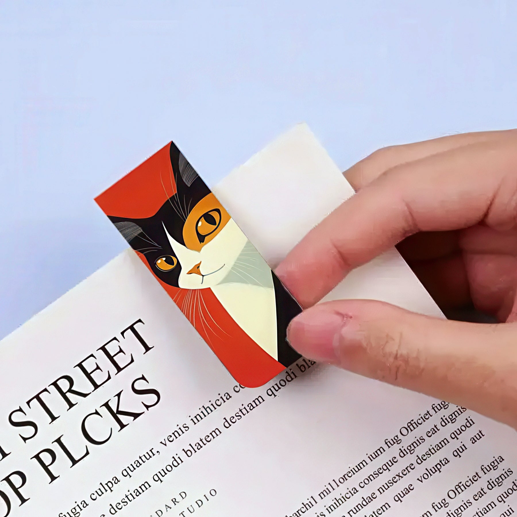 Cat-themed bookmark being held over a book with a light blue background
