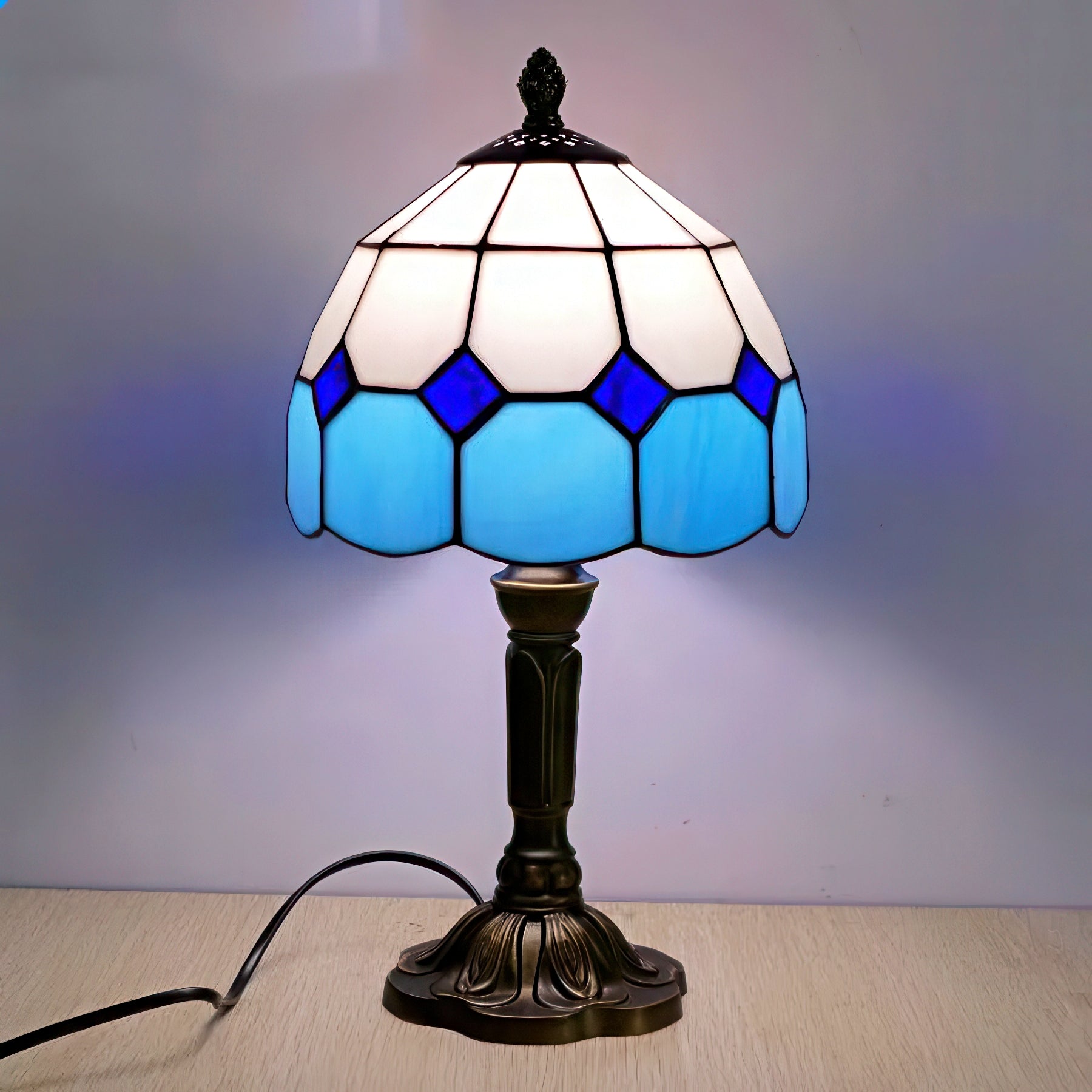 Tiffany-style table lamp with blue and white stained glass shade on a wooden surface.
