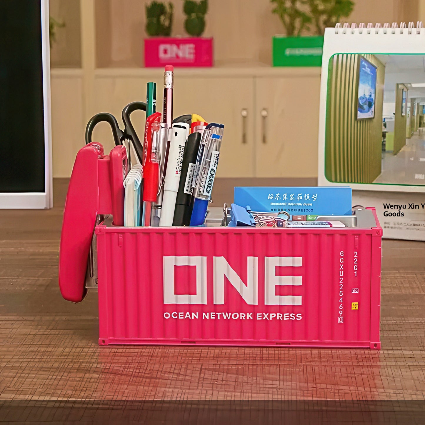 Pink container shaped pen holder with stationery items on a desk.
