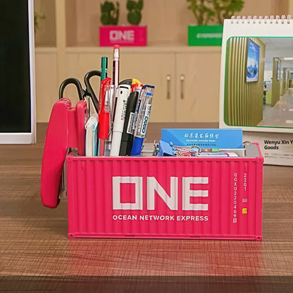 Pink container shaped pen holder with stationery items on a desk.