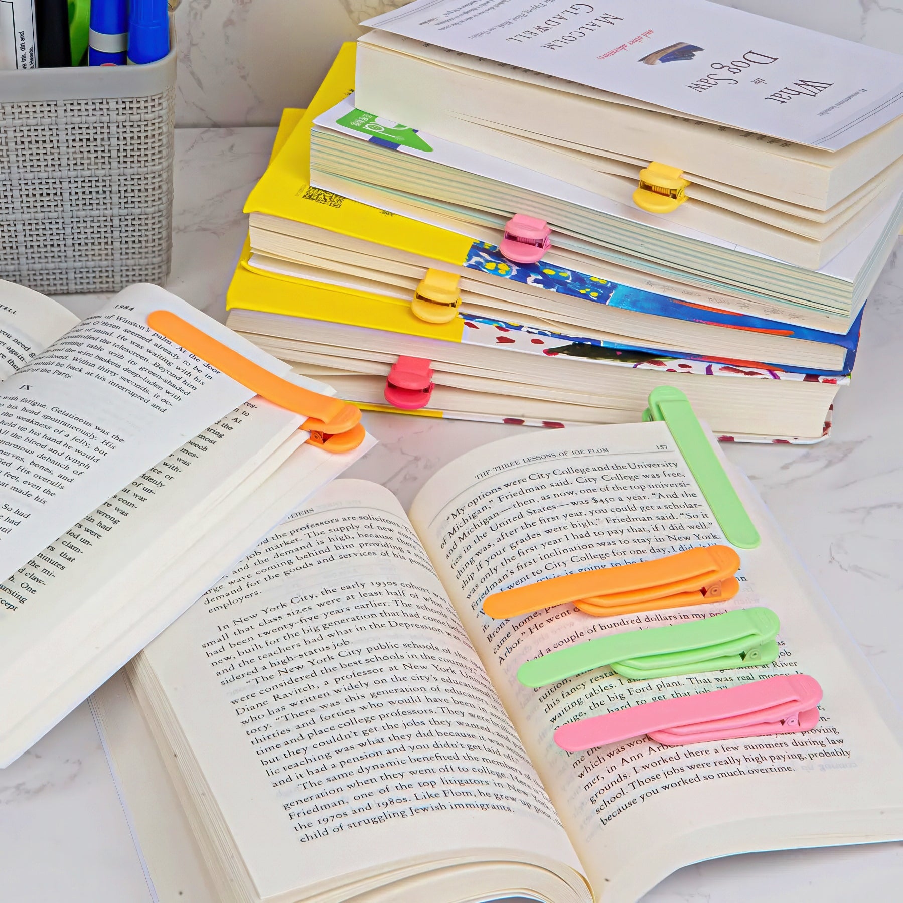 Colorful bookclips on open books with a stack of books in the background.