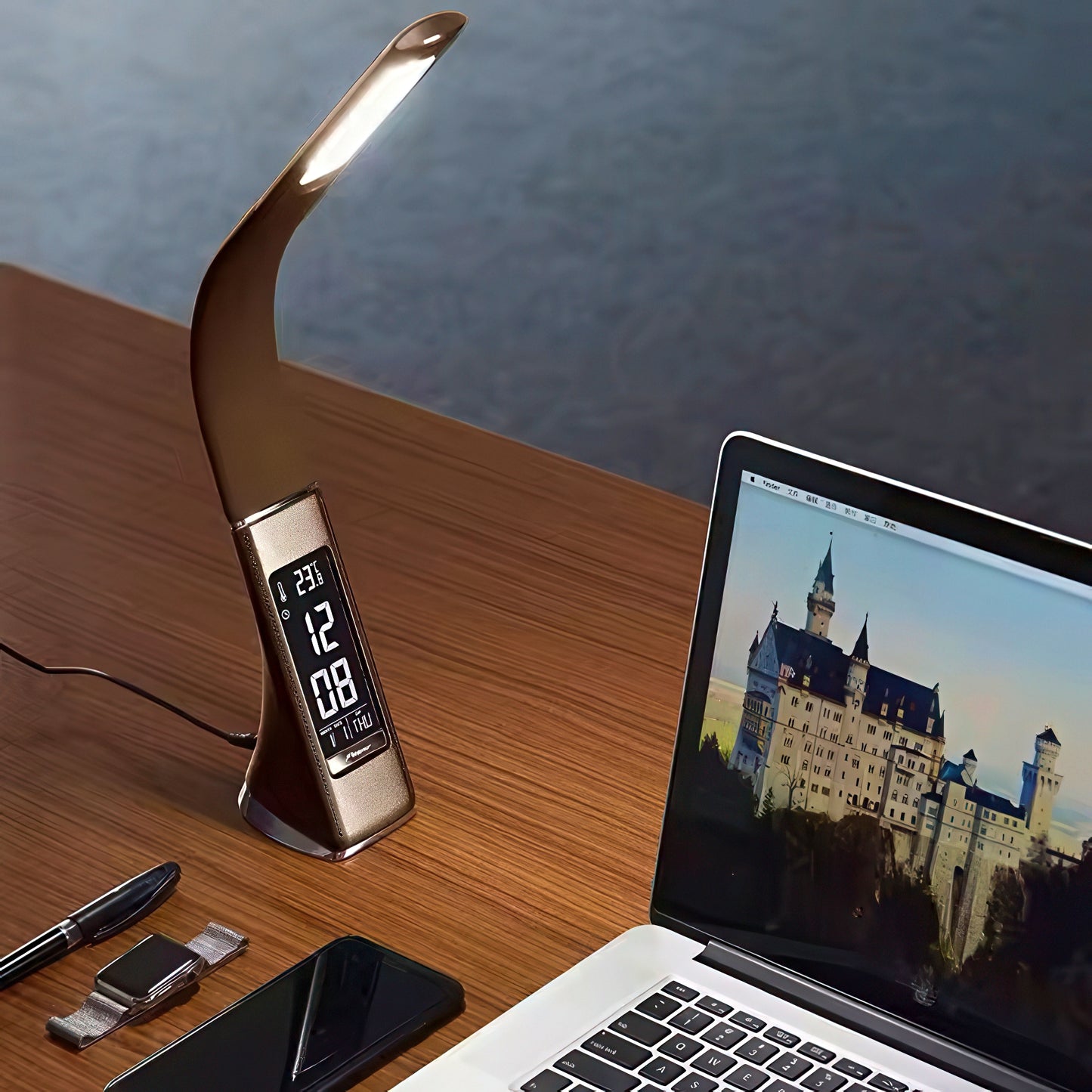 Desk setup with a flexible LED lamp, digital clock, smartphone, and laptop displaying a castle image.