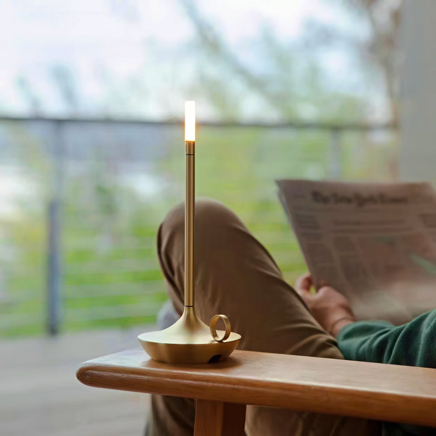 Person reading a newspaper with a gold candle holder shaped table lamp