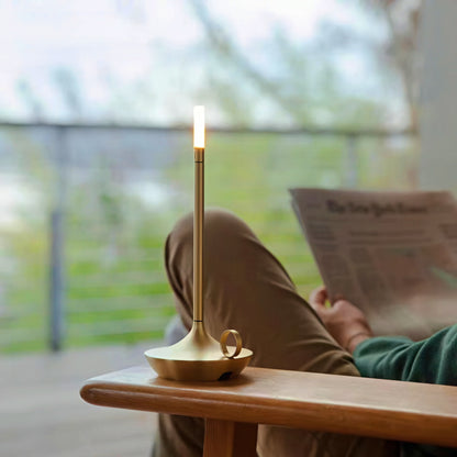 Person reading a newspaper with a gold candle holder shaped table lamp