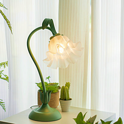 Decorative table lamp with floral design on a white surface, surrounded by plants.