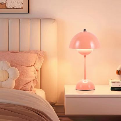 Pink table lamp on a nightstand next to a bed with floral pillows