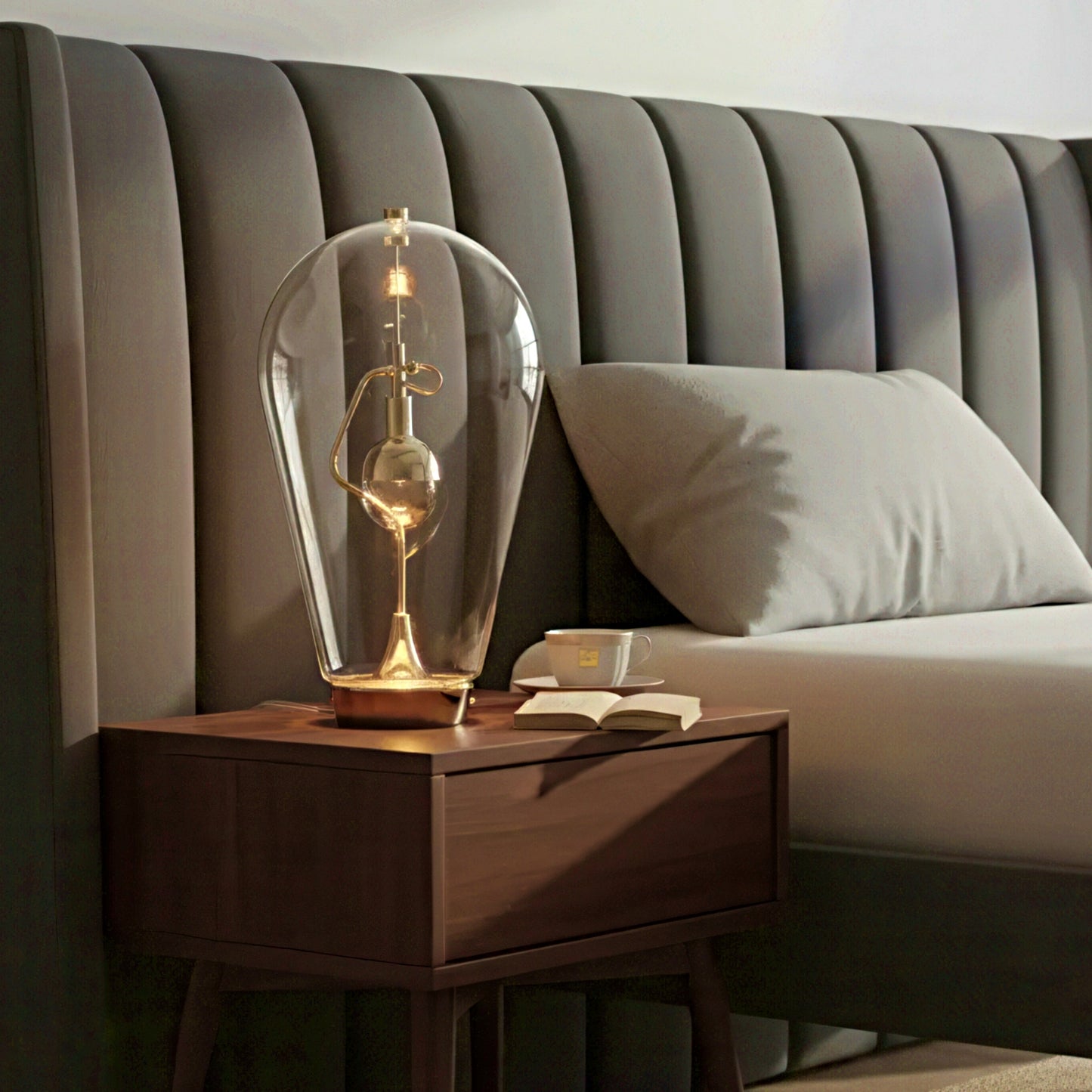 Wooden nightstand with a decorative lamp and book next to a bed with a tufted headboard.