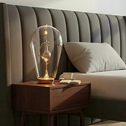 Wooden nightstand with a decorative lamp and book next to a bed with a tufted headboard.
