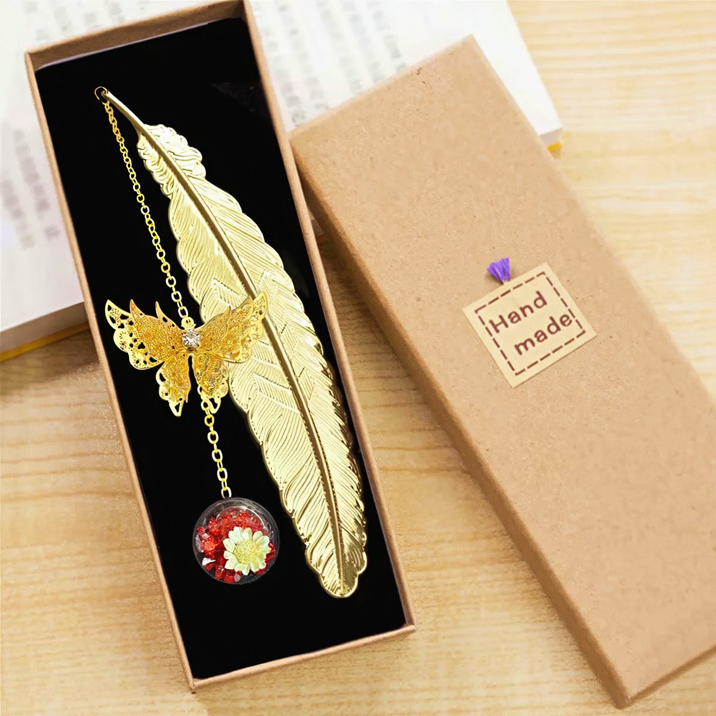 Gold feather shaped bookmark with butterfly pendant in a box.