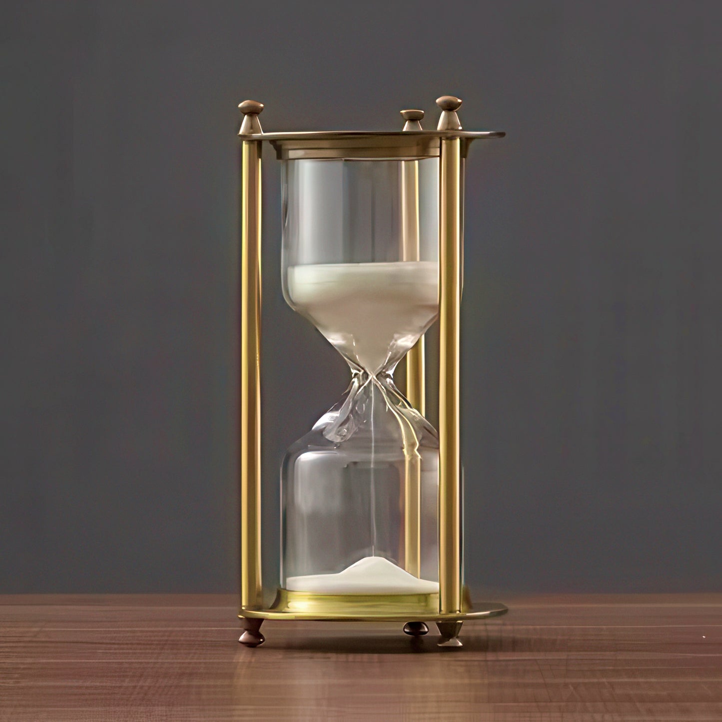 Gold-framed hourglass with sand on a wooden surface and dark background