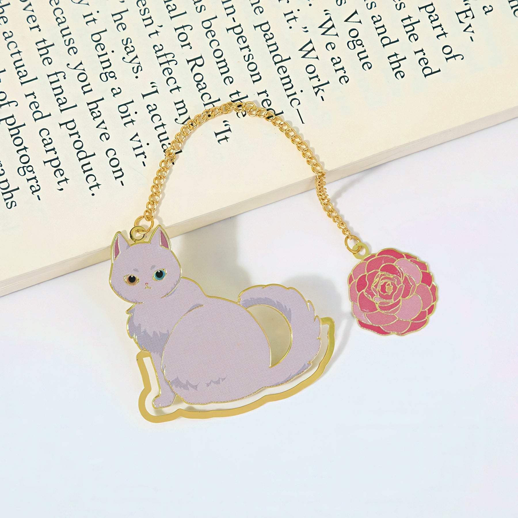 Cat-shaped metal bookmark with a pink rose charm on a white surface