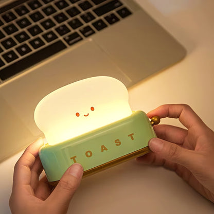 Person holding a cute toaster-shaped night light with a smiling face, illuminated, in front of a laptop.