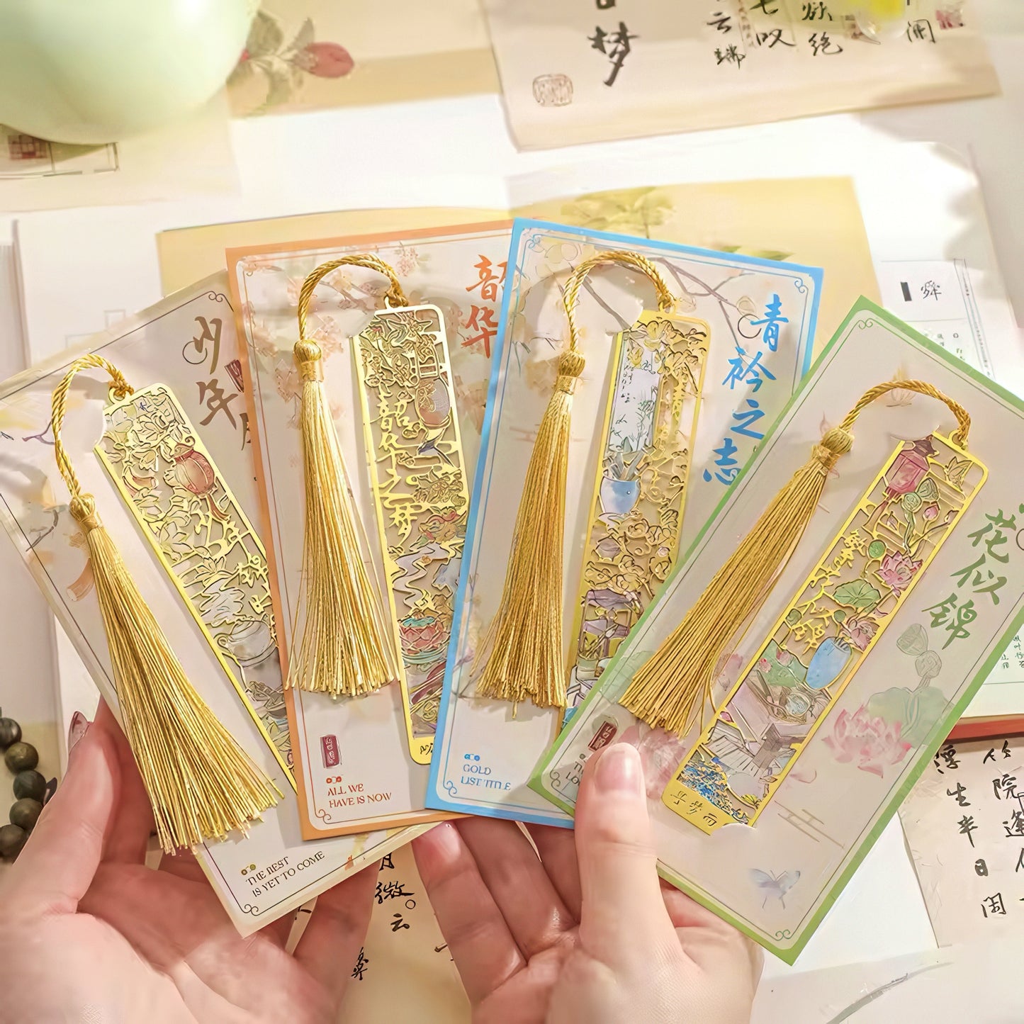 Gold tassel bookmarks held by hands with a decorative background
