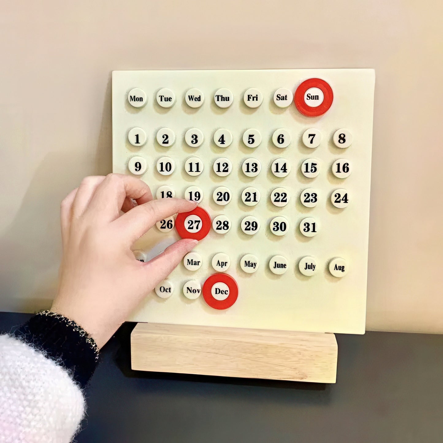 Calendar with plastic buttons being pressed by a hand on a neutral background