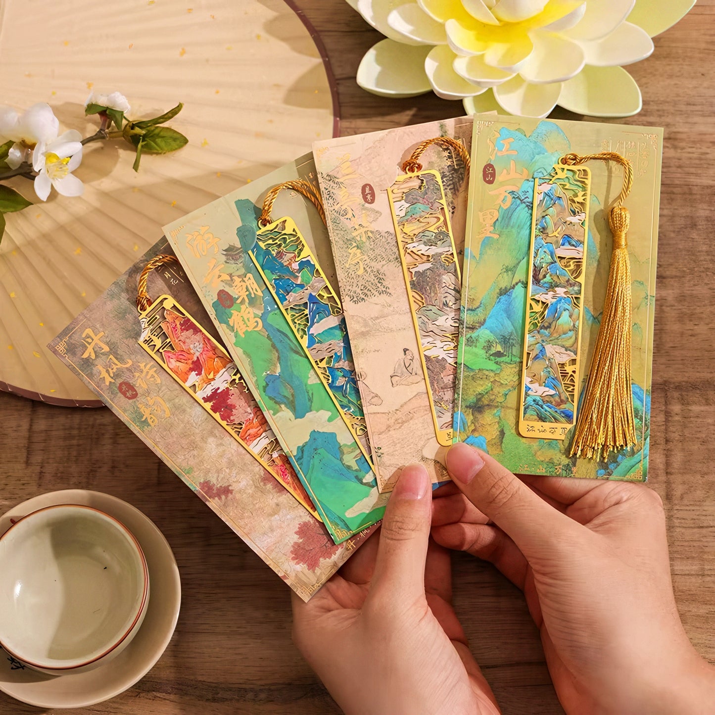 Metal bookmarks with tassels held by hands on a wooden surface.