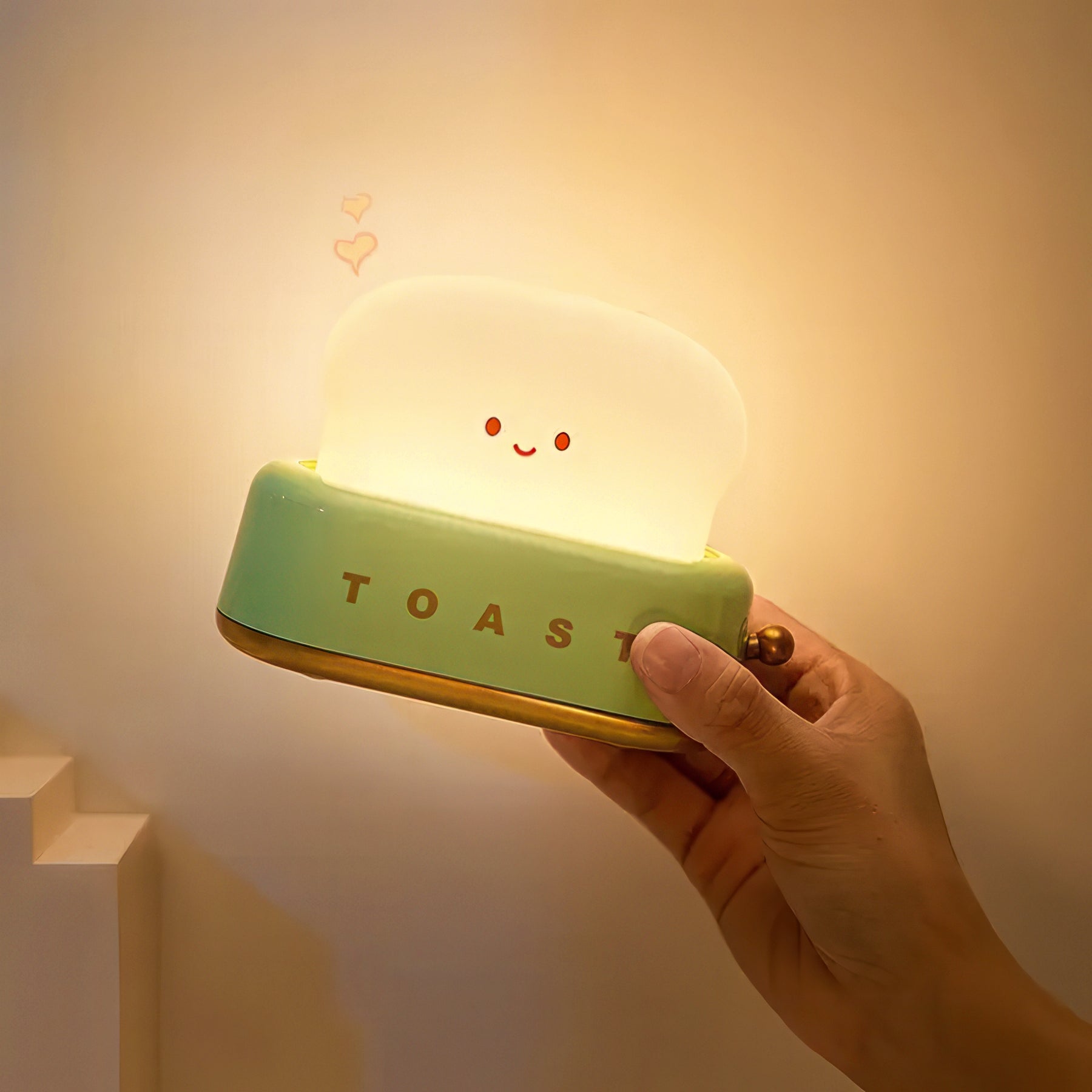 Hand holding a glowing night light shaped like a toaster with a smiling face.