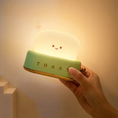 Hand holding a glowing night light shaped like a toaster with a smiling face.
