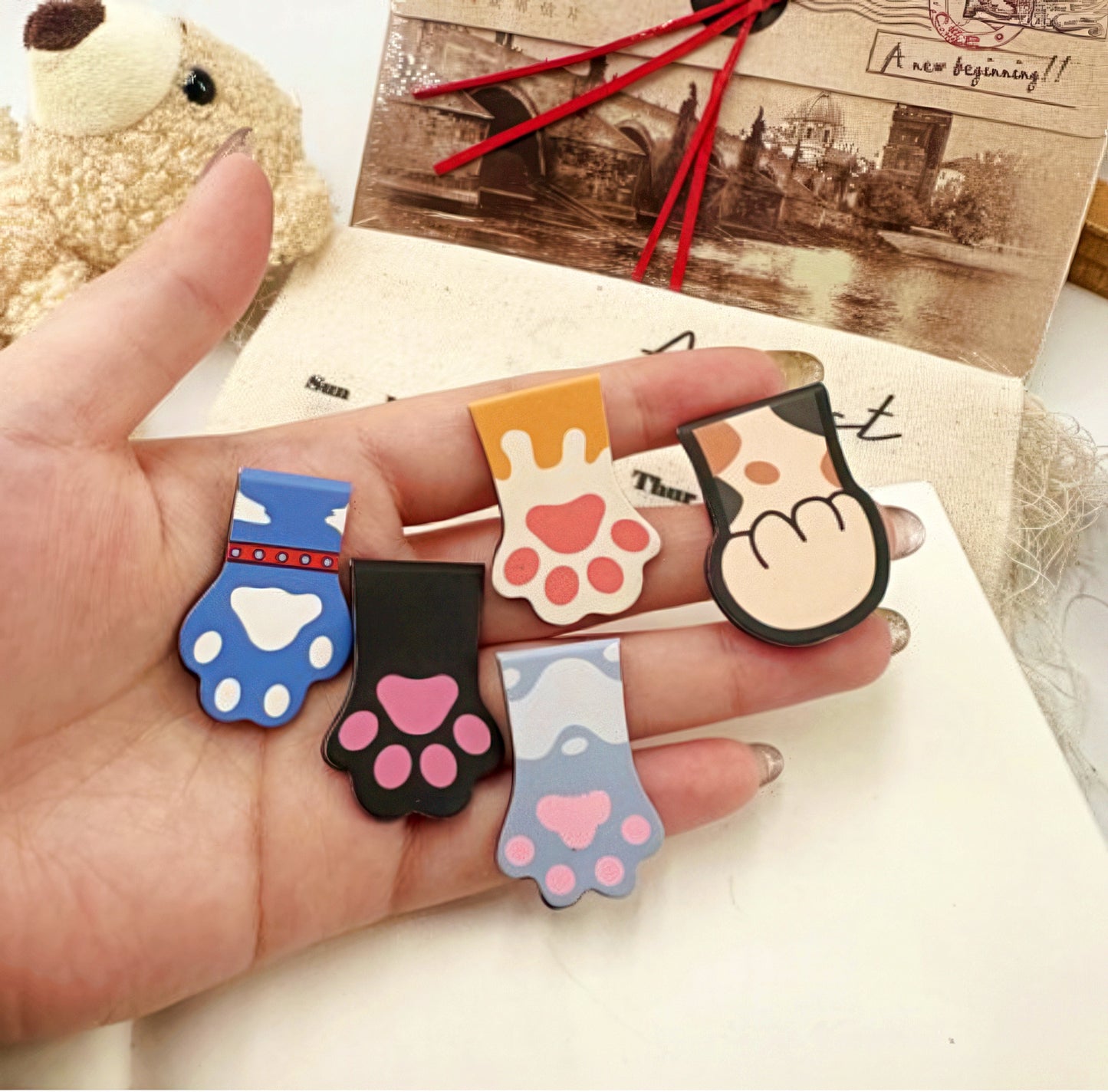 Hand holding five cat paw shaped bookmarks.
