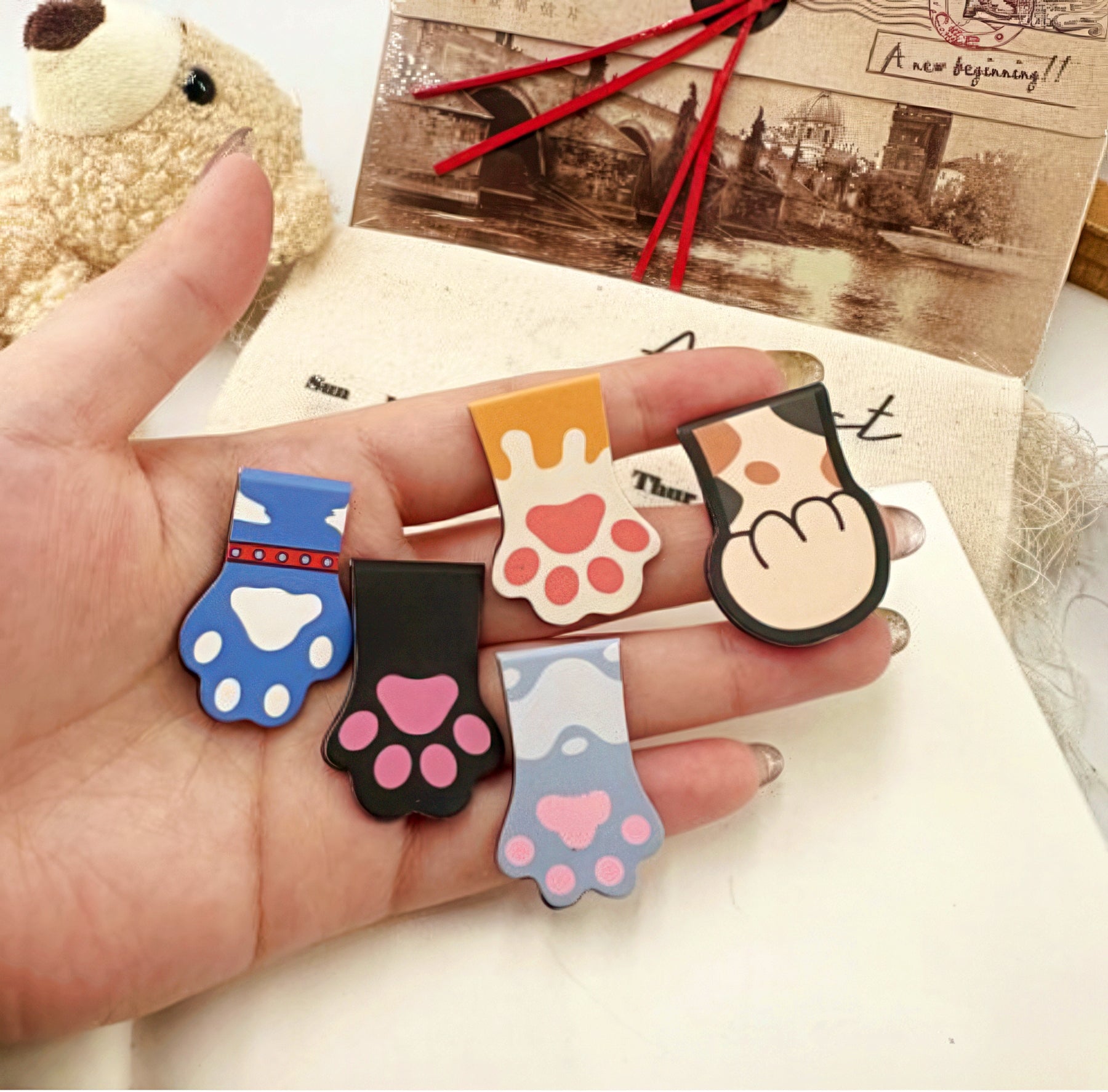 Hand holding five cat paw shaped bookmarks.