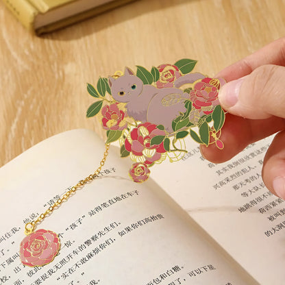 Decorative bookmark with a cat and flowers held over an open book.